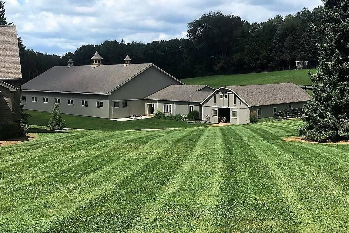 Country farmhouse with green striped lawn and trees under a cloudy sky