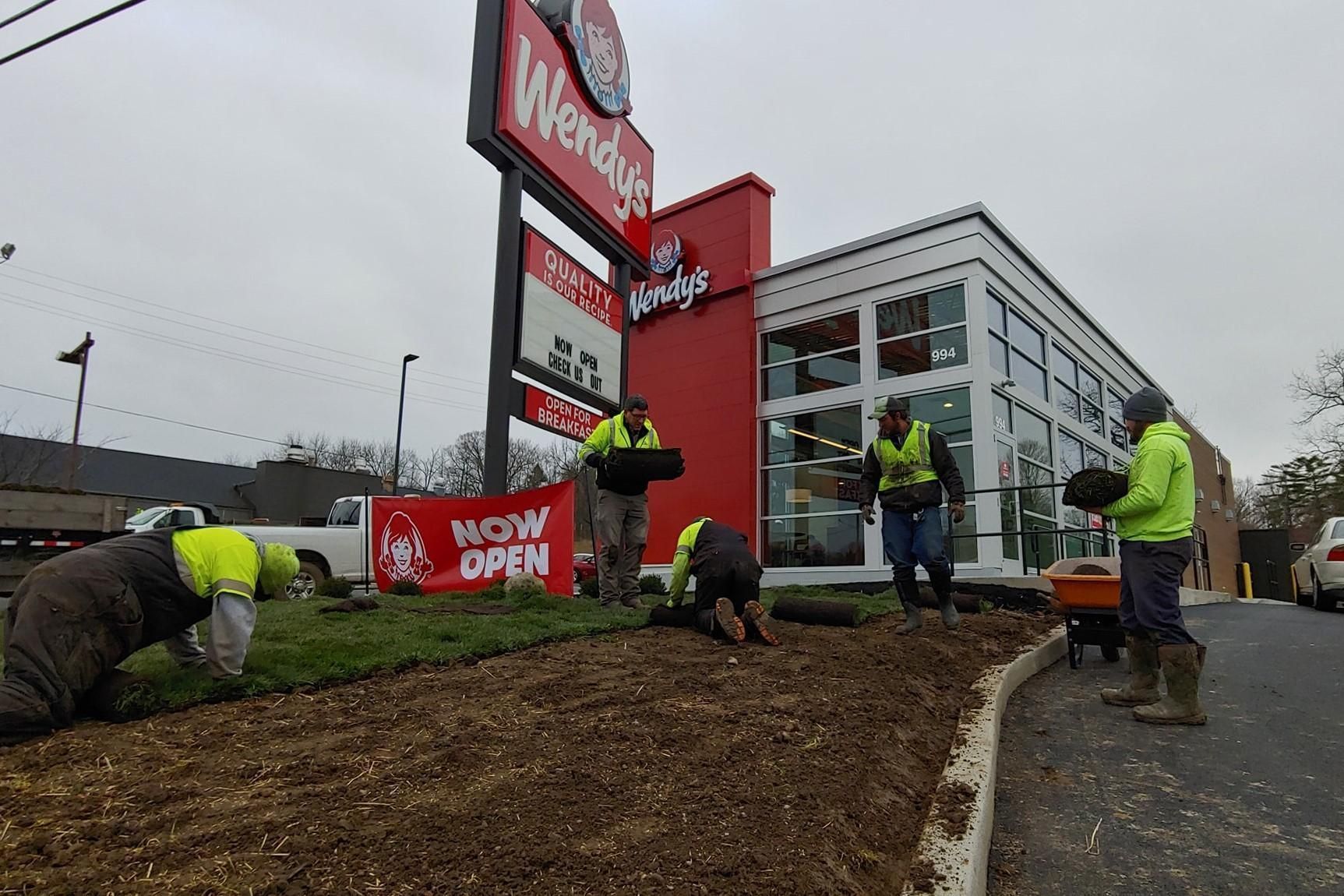 Workers install a red Wegmans sign outside a new store under gray skies.