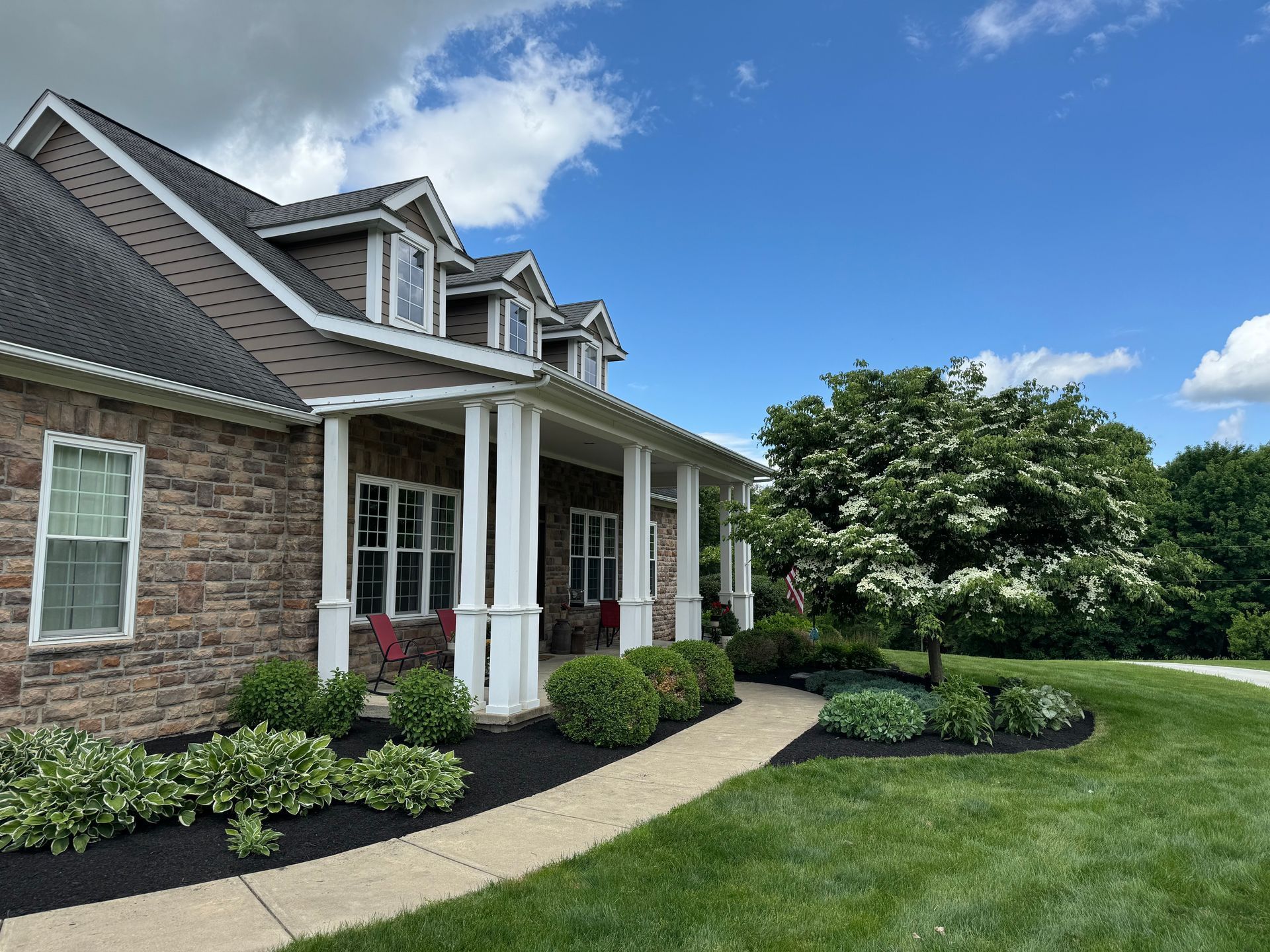 Brick suburban house with white columns, front porch, curved walkway, and manicured lawn under a blue sky