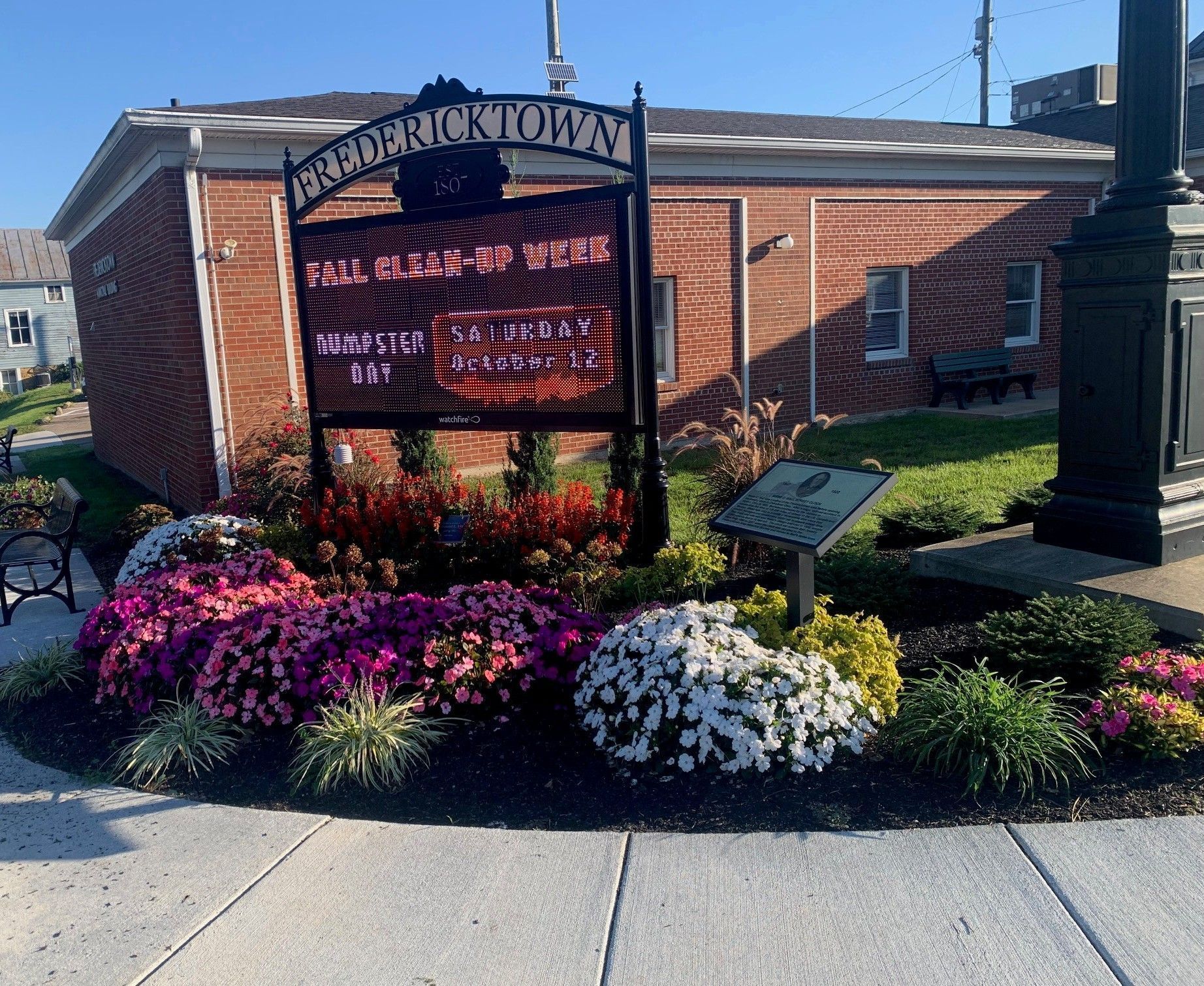 Ornamental sign with colorful flowers in front of a brick building on a sunny street corner
