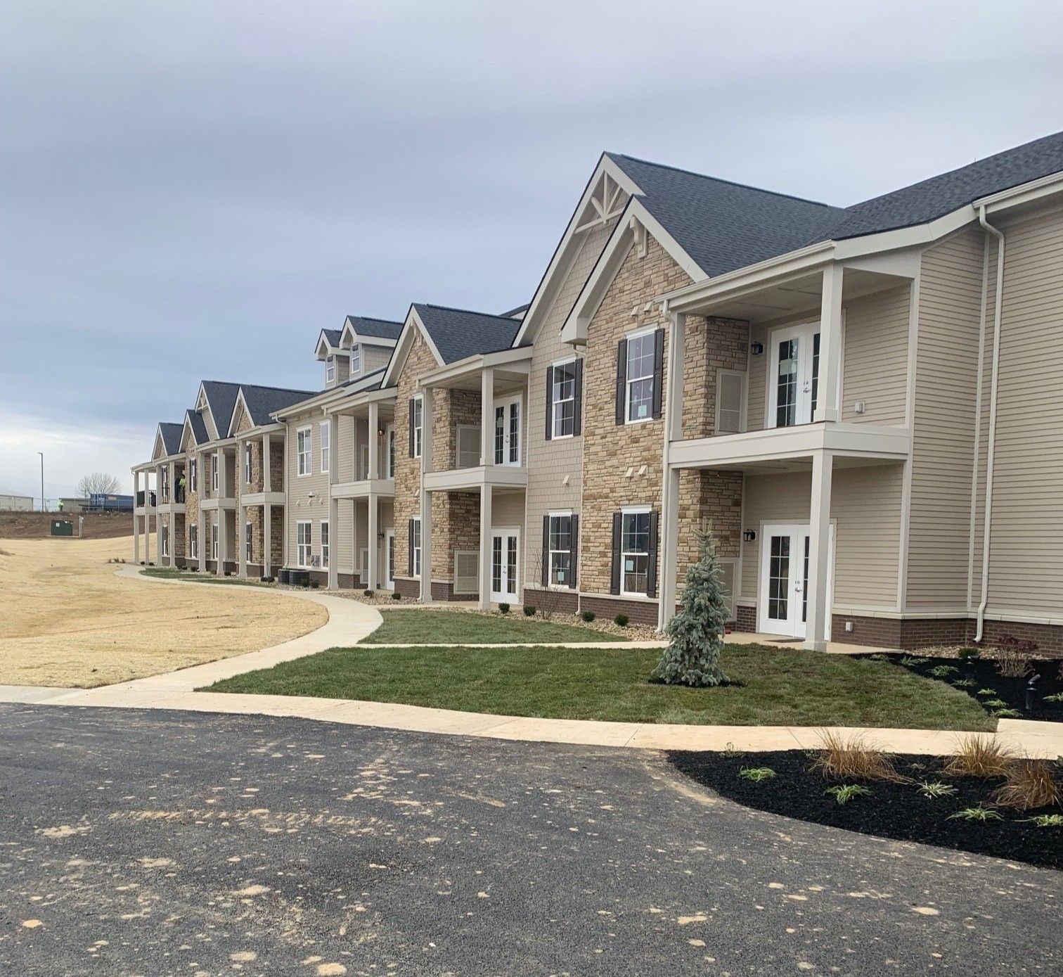 Row of beige apartment buildings with balconies beside a paved path and grassy lawn