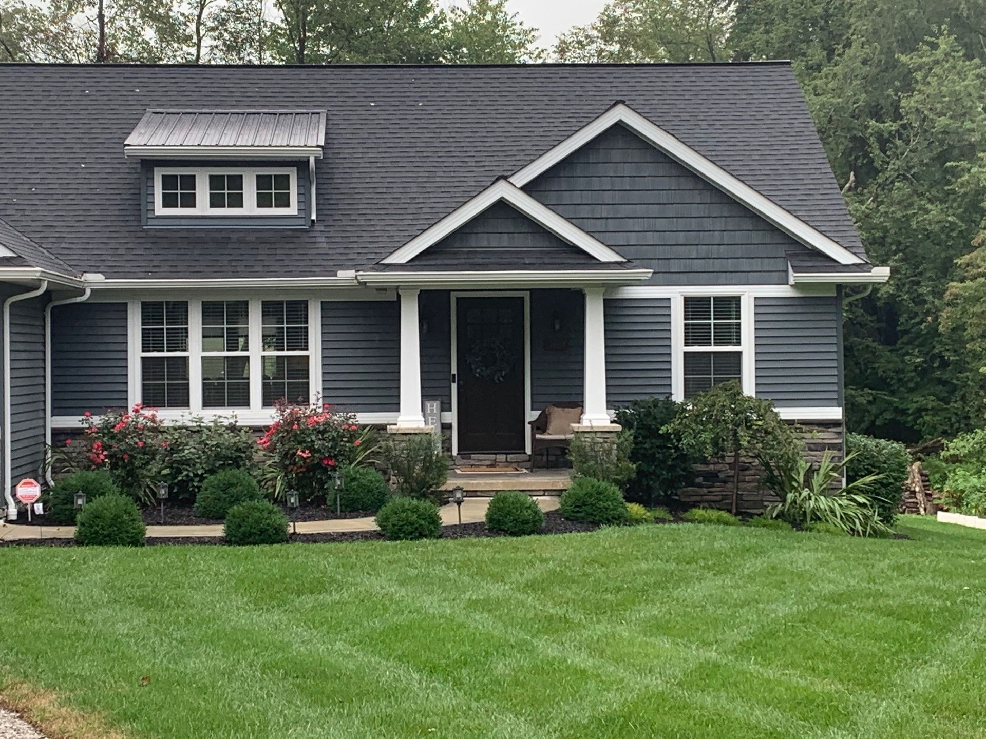 Dark gray house with white trim, a front porch, and a neatly manicured green lawn.