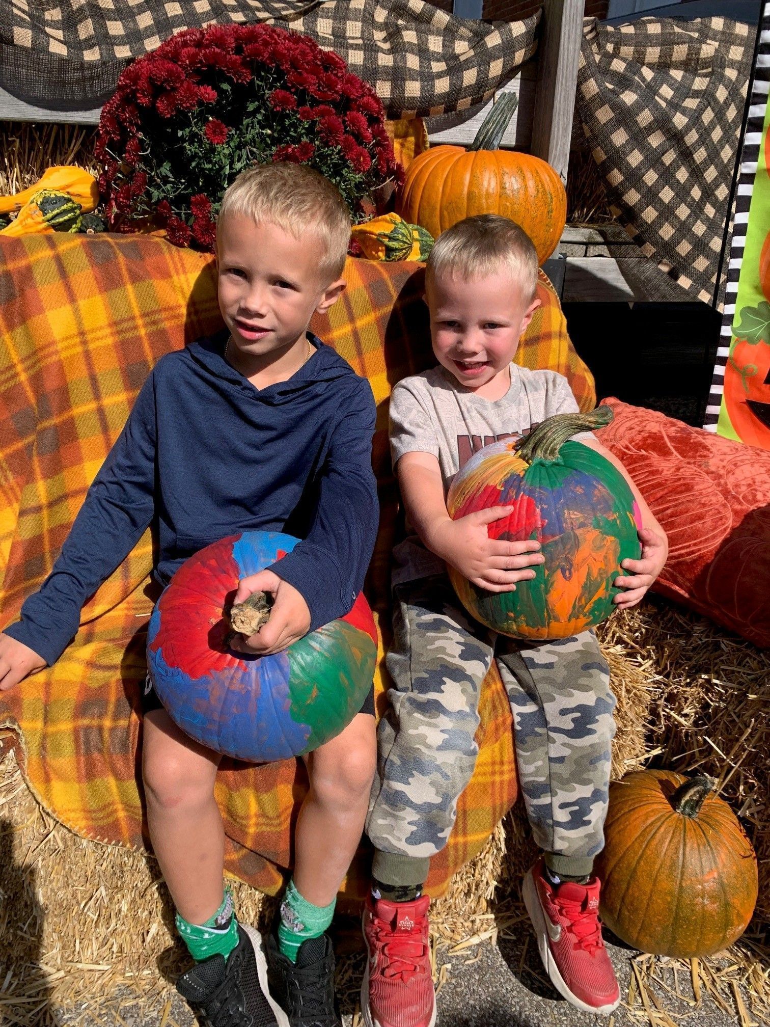 Two children sitting on hay bales holding colorful pumpkins at a fall festival