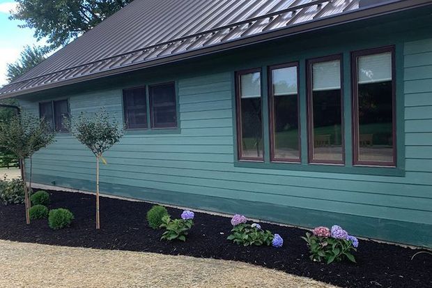 Green house exterior with dark roof, windows, and a landscaped garden bed with flowers.