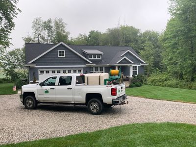 White pickup truck parked on a gravel driveway in front of a gray house surrounded by trees