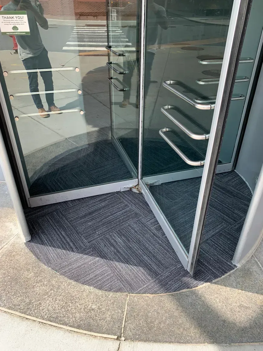 Revolving glass door with gray carpet flooring at building entrance.