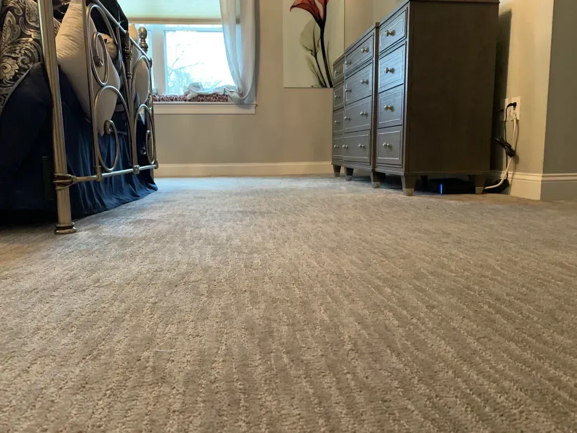 Low-angle view of a gray carpeted bedroom with a bed on the left and dresser on the right.
