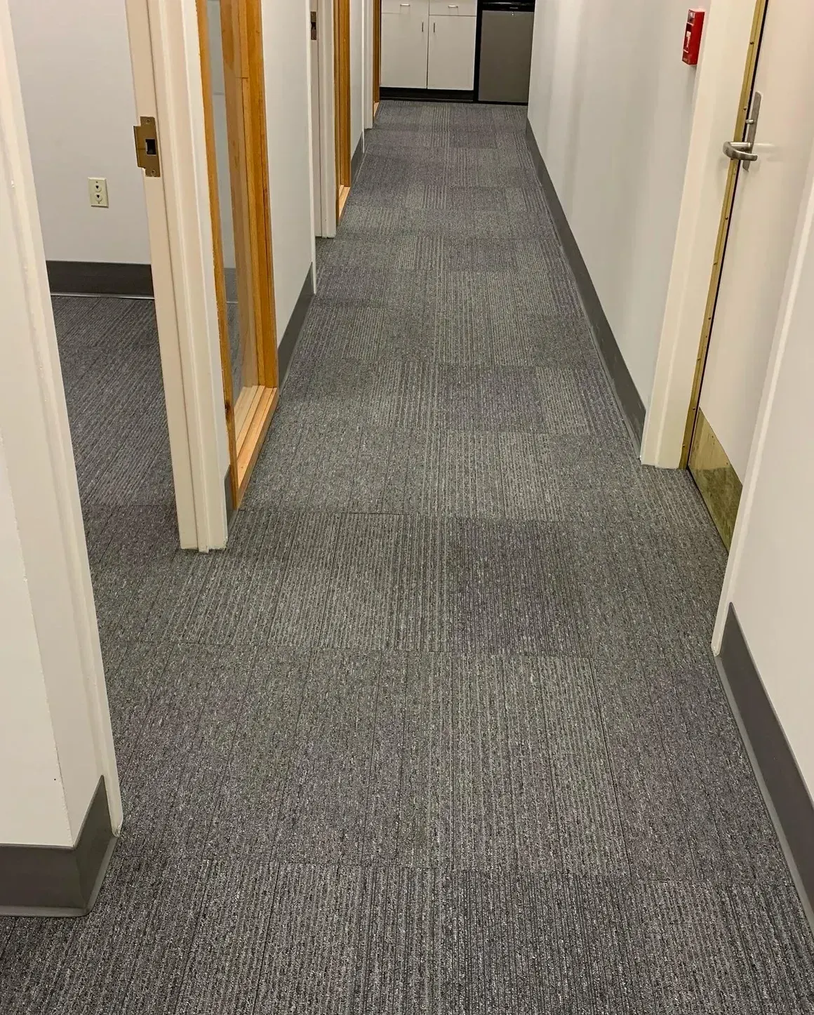 Narrow office hallway with gray carpet, white walls, and open doors.