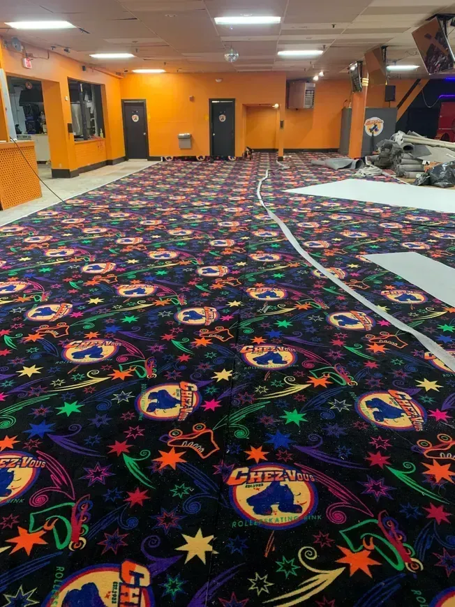 Roller rink interior with patterned carpet and orange walls. Construction materials visible.