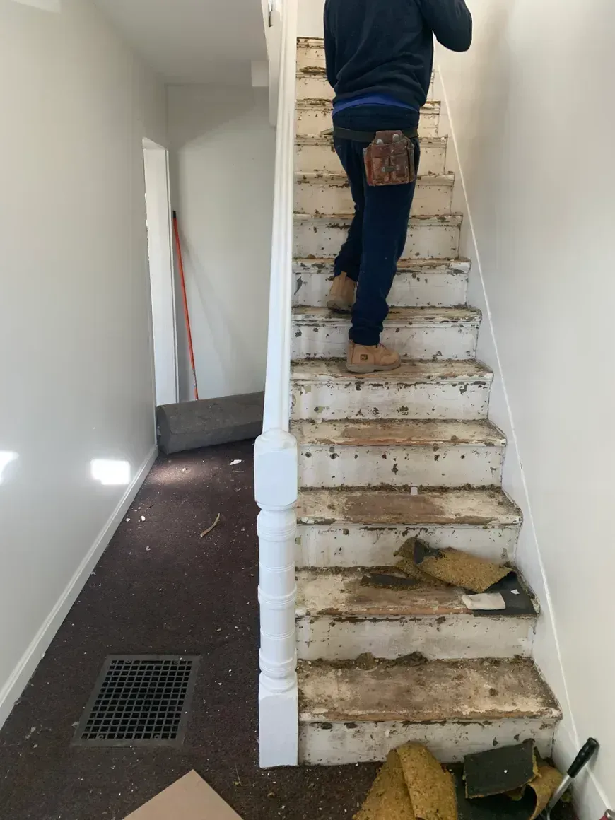 Person climbing a staircase with damaged treads and carpet removal debris.