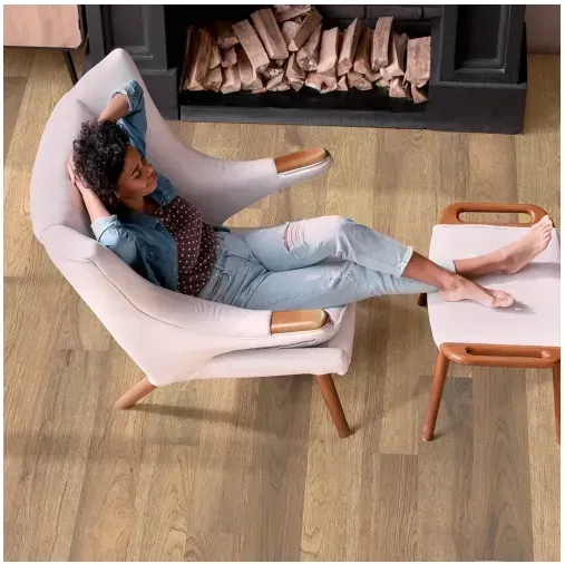Woman reclining in a white chair, feet up on a stool, by a fireplace.