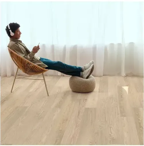 Person seated in a chair, wearing headphones, using a phone near a window with a footrest.