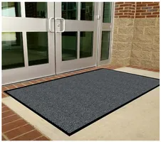 Gray commercial door mat in front of glass doors, on a brick and concrete building.