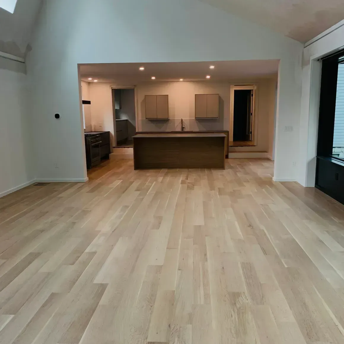 Empty, light-floored kitchen with island and cabinetry; view through an archway.