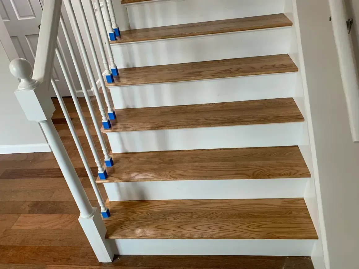 Wooden staircase with white risers and railing, blue tape on steps.