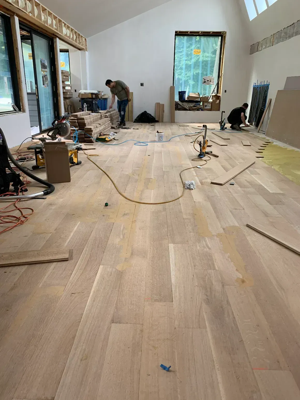 Workers installing wood flooring in a room with large windows.
