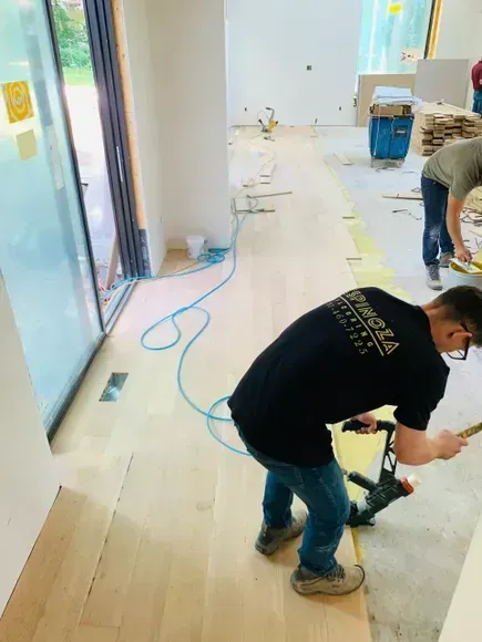 Man installing wood flooring with a nail gun in a room under construction.