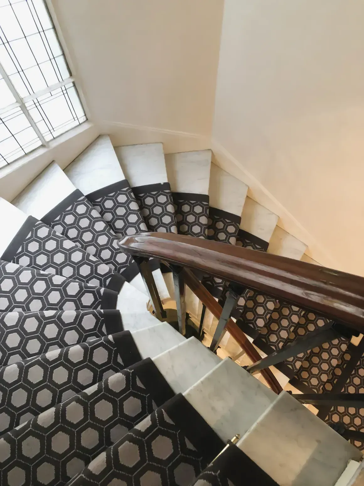 Staircase with patterned runner, wood banister, and window.