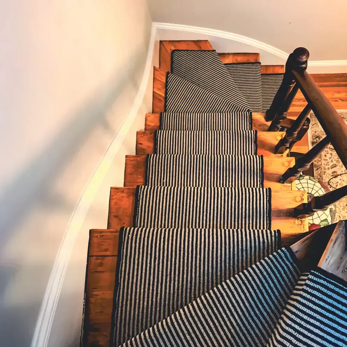 Wooden staircase with black and white striped runner, viewed from above.