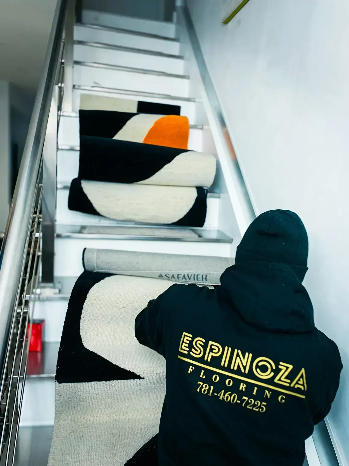 Man carrying rolled-up rugs on staircase, wearing 