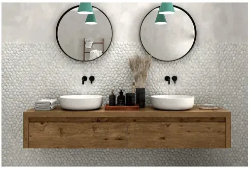 Bathroom with double vanity, two round mirrors, pebble tile backsplash, and wood floating cabinet.