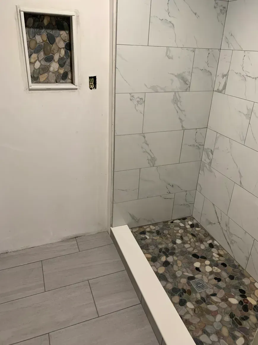 Shower stall with pebble floor and marble-look wall tiles; a niche with decorative stone.