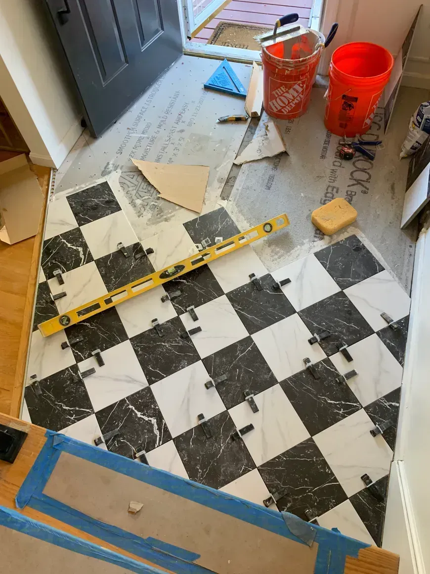 Black and white checkered tile floor being installed near a doorway with tools like a level and buckets.