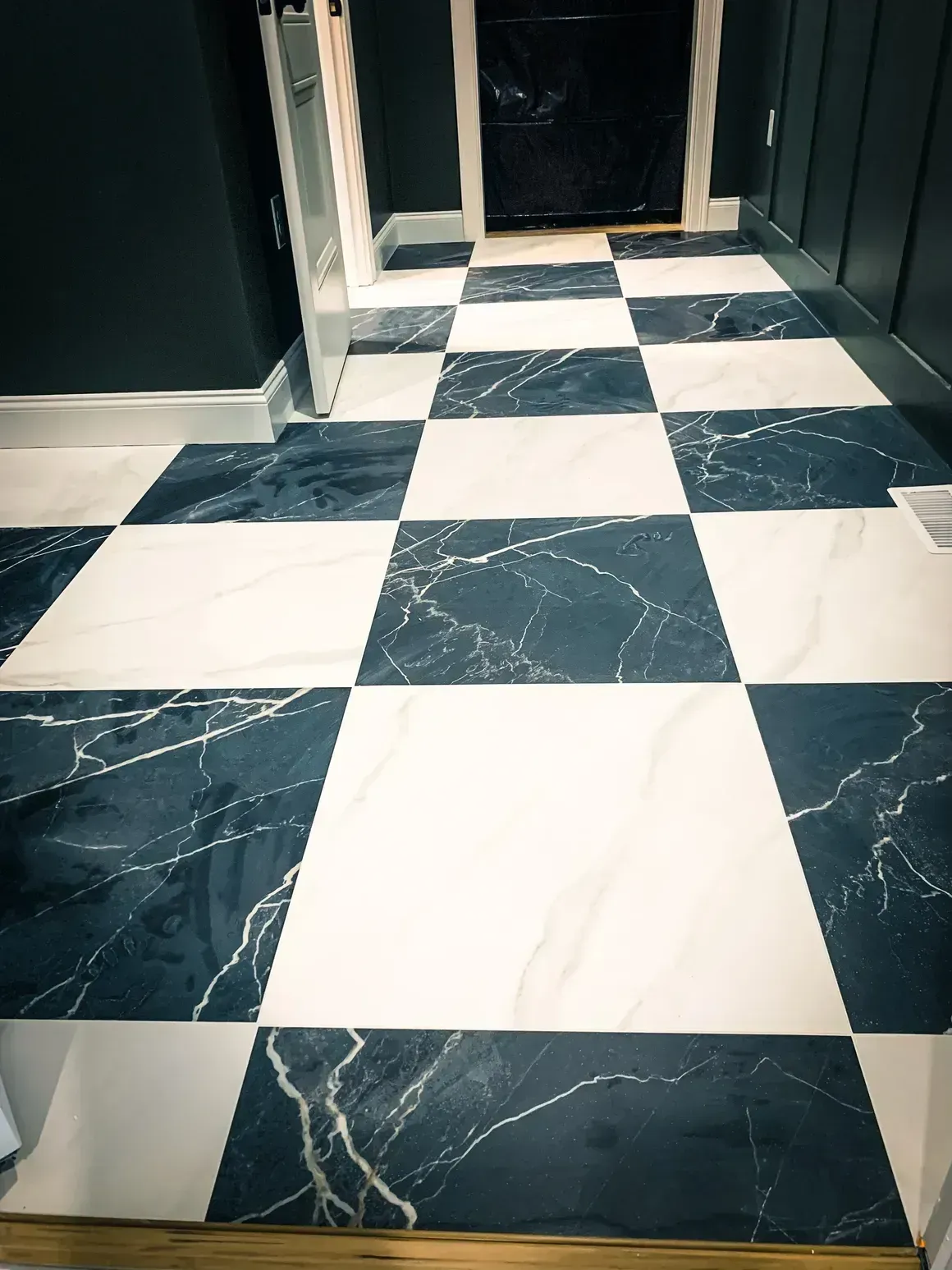 Black and white checkered marble floor in a hallway with dark walls and a closed black door.