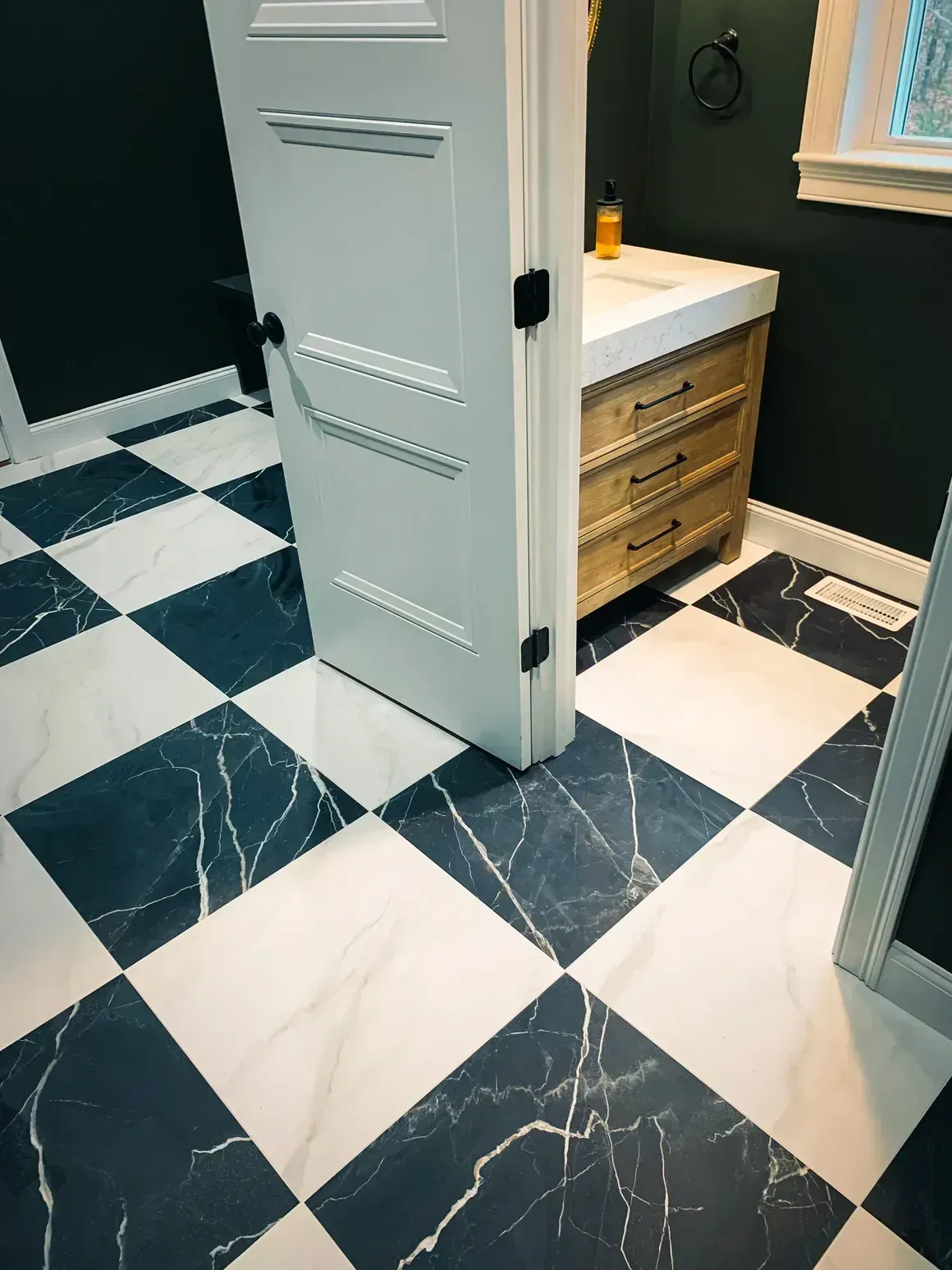 Bathroom with checkered black and white marble floor, white door, and wooden vanity.