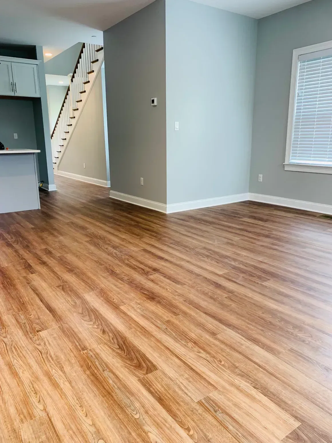 Empty interior room with hardwood-style flooring, gray walls, and a staircase in the background.