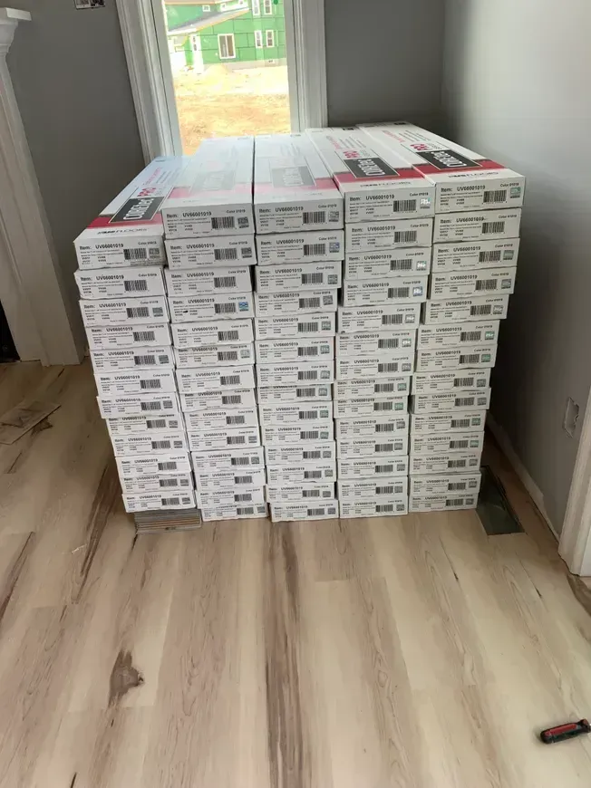 Stack of flooring boxes in a room with a light wood floor and a window.