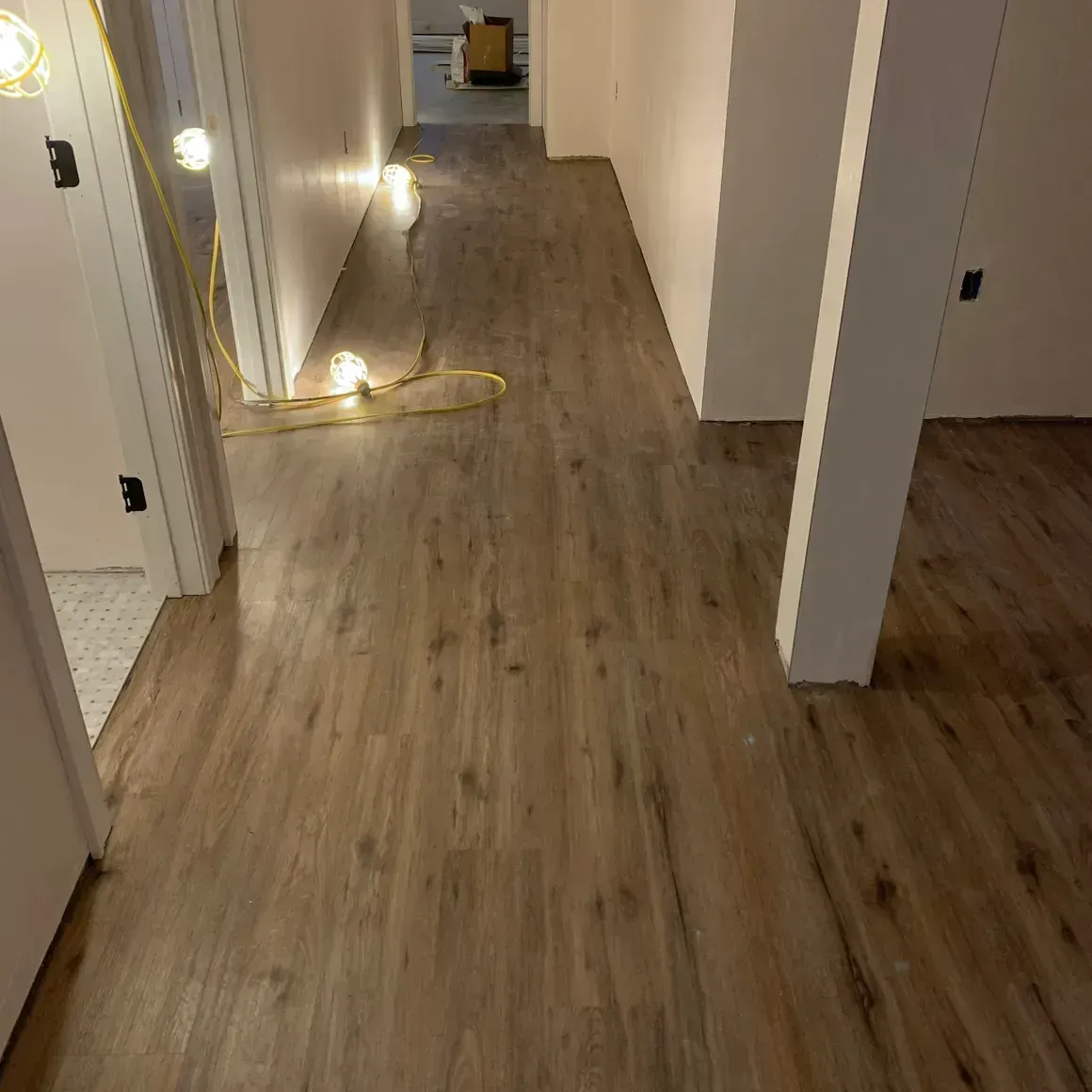Hallway with newly installed wood-look flooring and white walls, construction in progress.