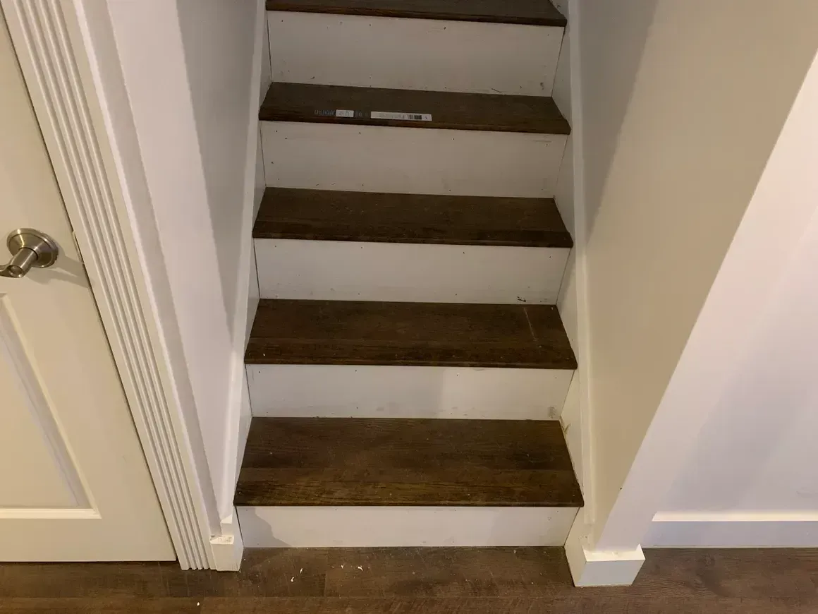 Staircase with wooden steps and white risers and trim between white walls.