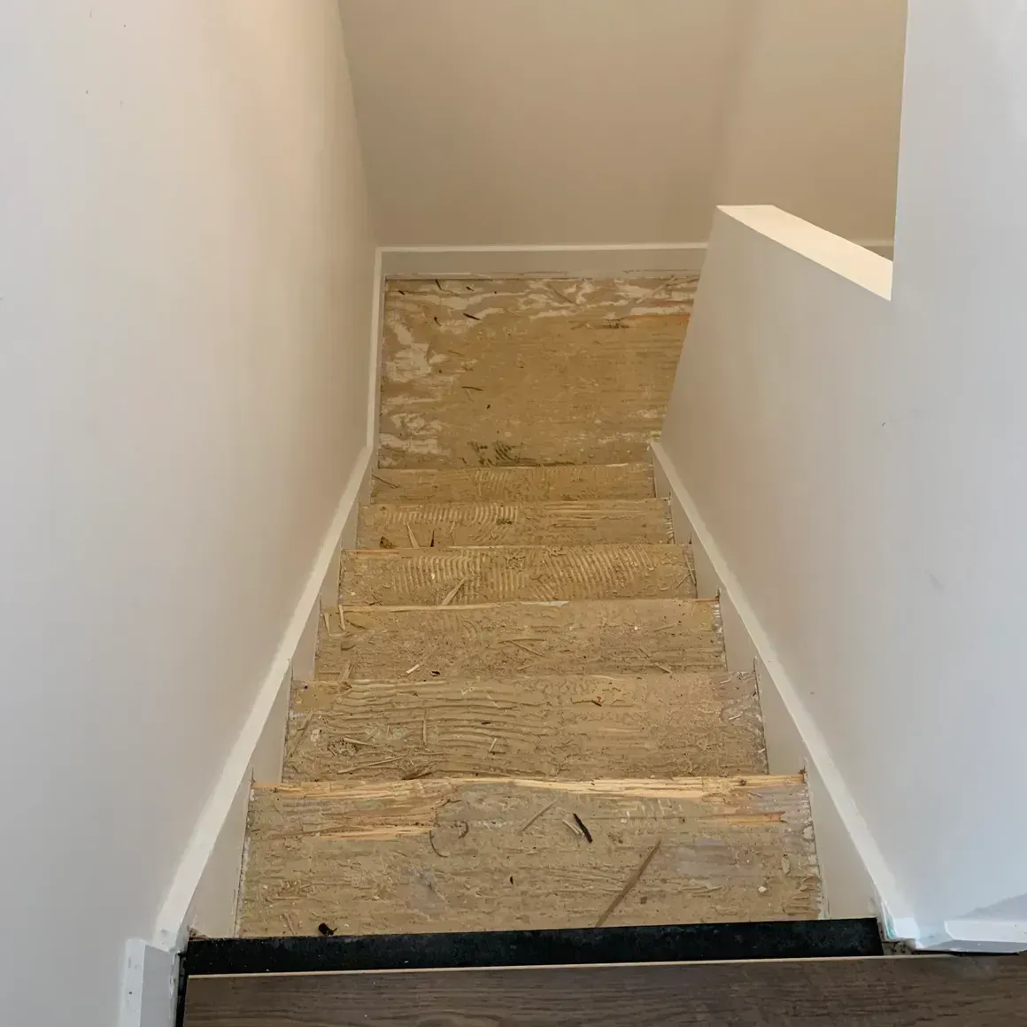 Staircase with exposed wood steps, white walls and trim, leading downwards.