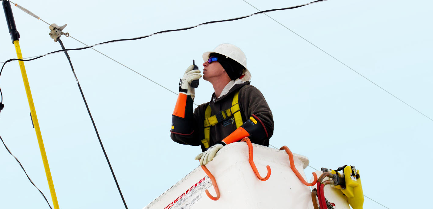 A man is standing on top of a power pole talking on a cell phone.