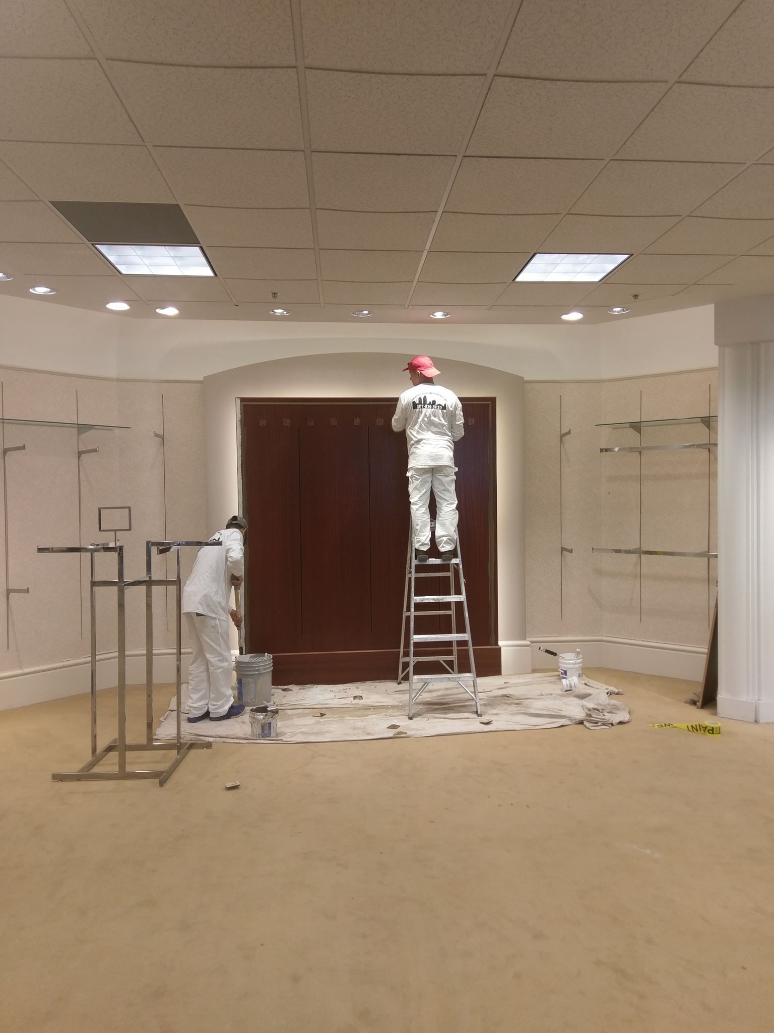 A man on a ladder paints a wall in an empty room
