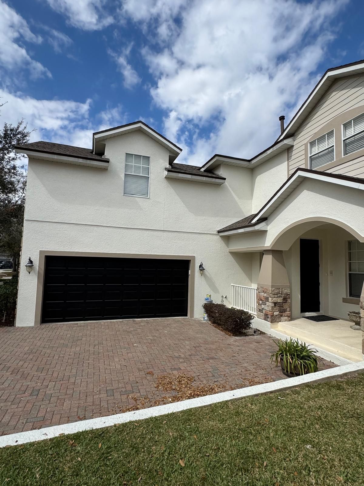 A large white house with a black garage door and a brick driveway.