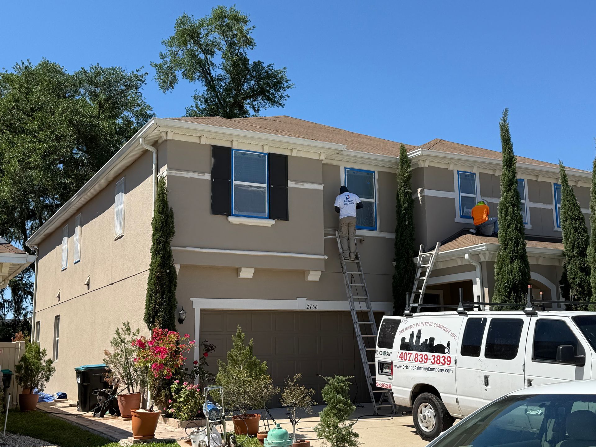A man on a ladder is painting the windows of a house.