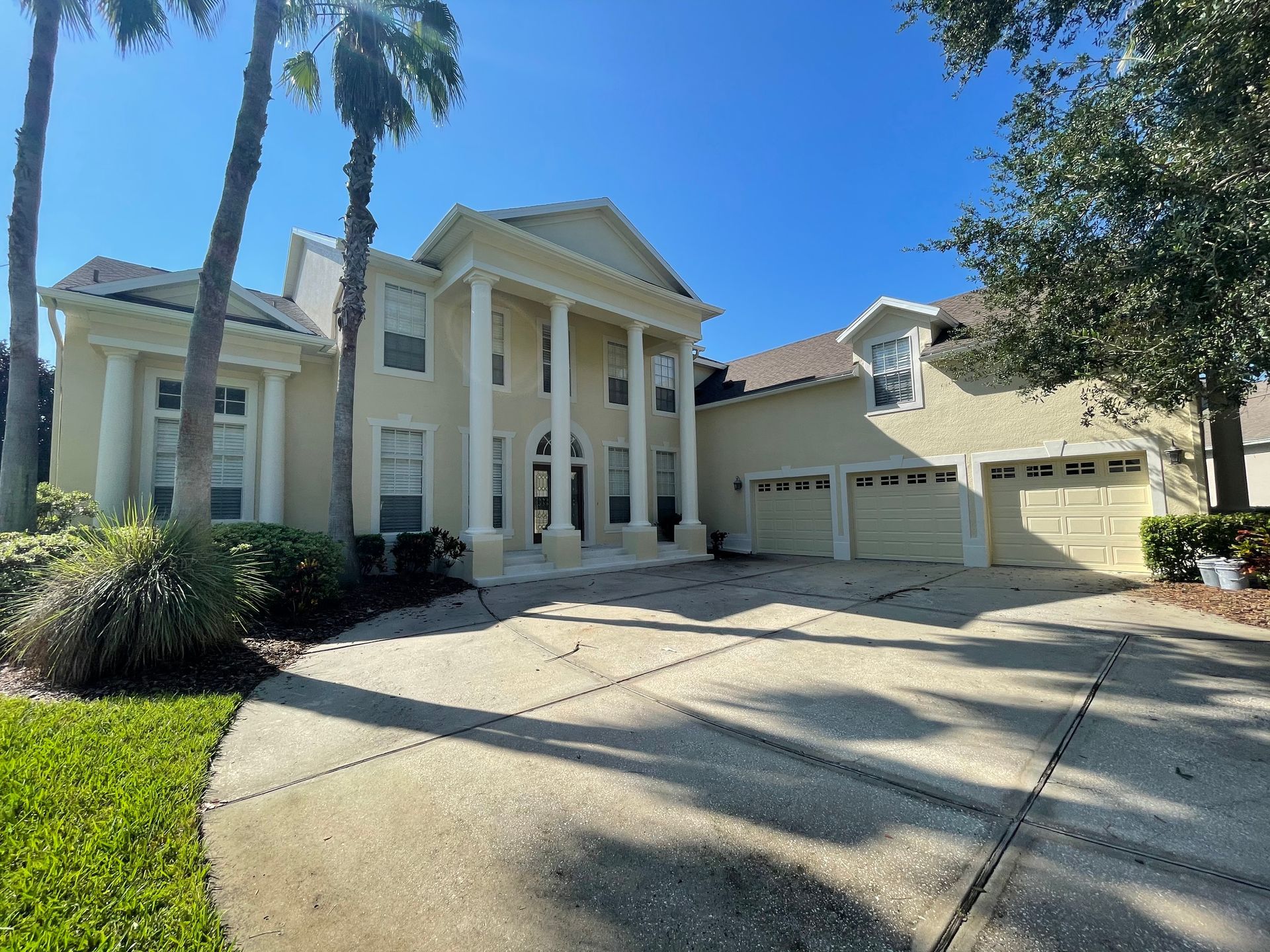 A large white house with two garages and palm trees in front of it