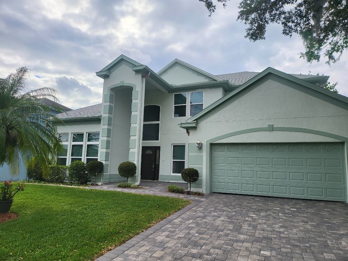 A large white house with a green garage door and a brick driveway.