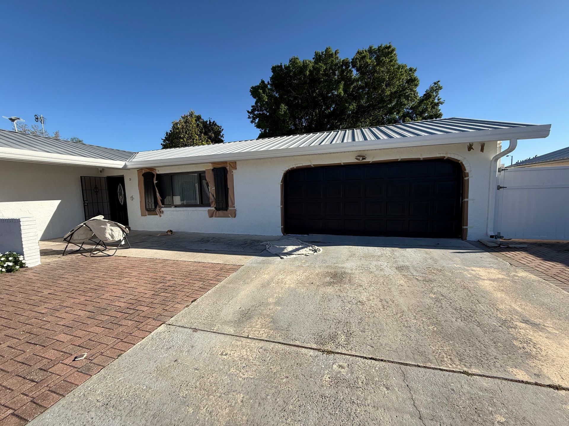 A white house with a black garage door and a brick driveway.