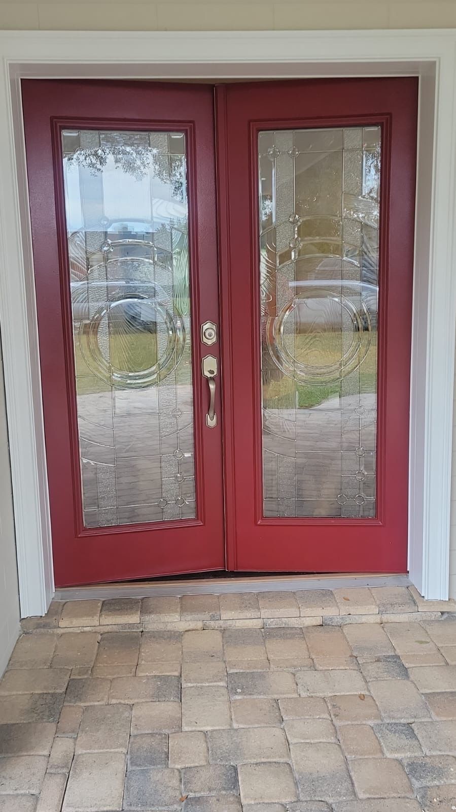 A red door with stained-glass is sitting on a brick porch.