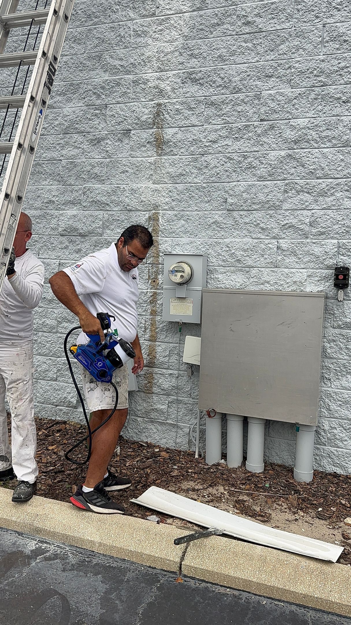 Two men are painting a brick wall with a ladder.