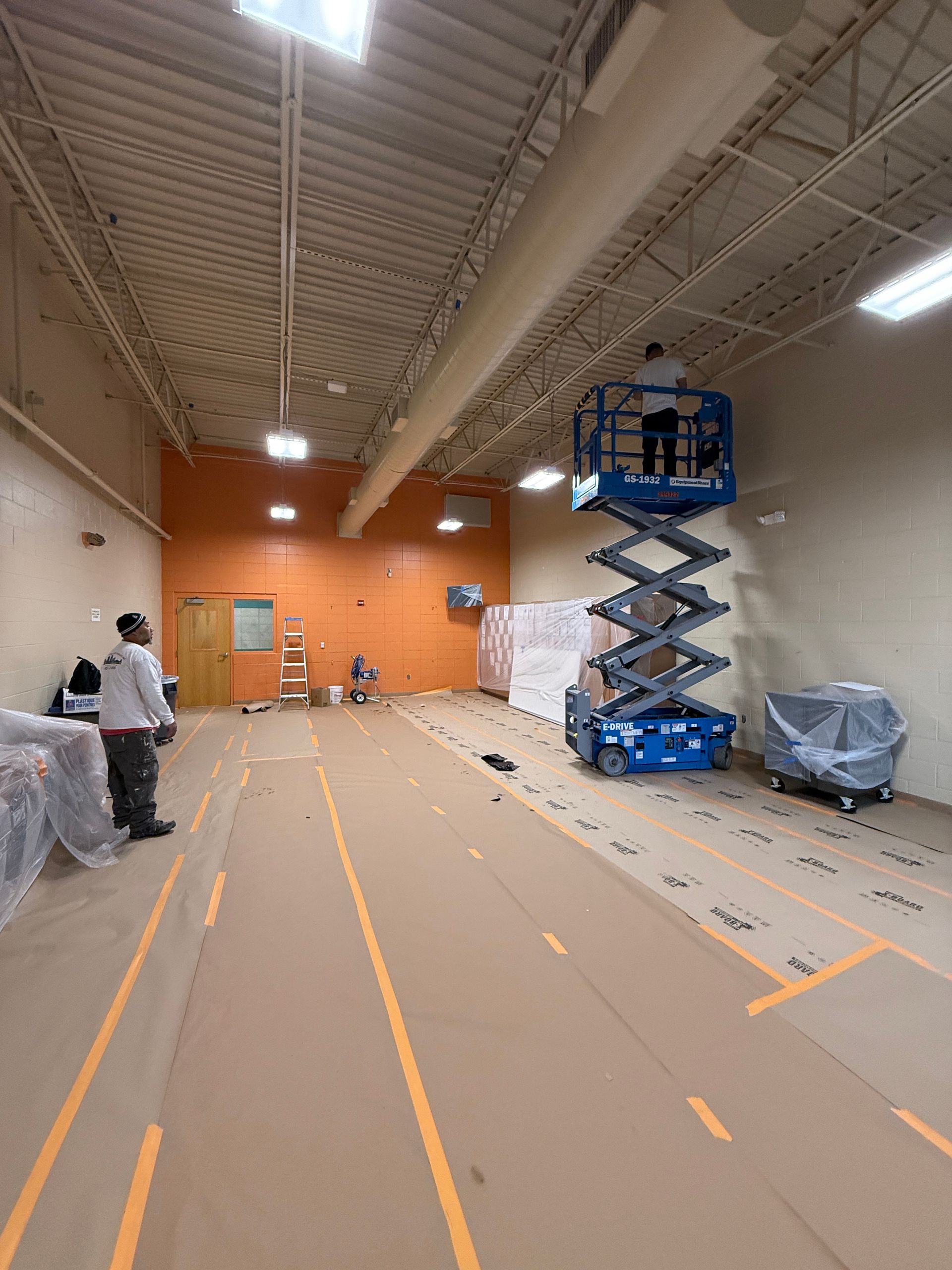 A man is standing on a scissor lift in a large room.