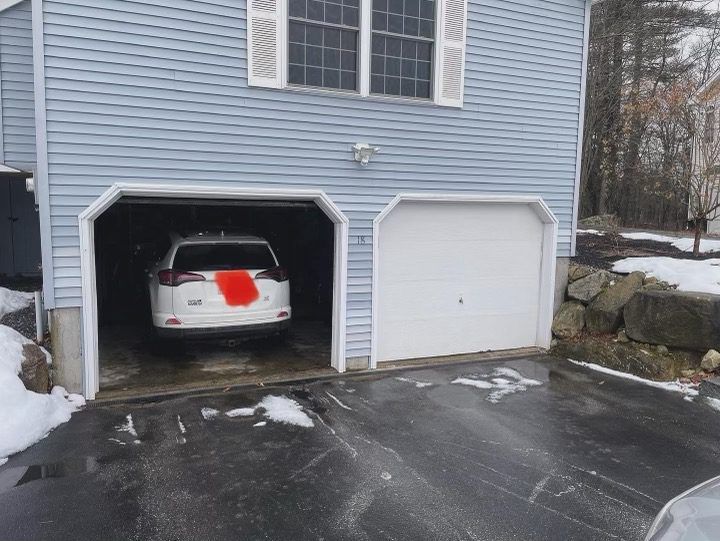 A two-car garage under a blue-sided house with snow on the ground; one bay is open with a white SUV inside.