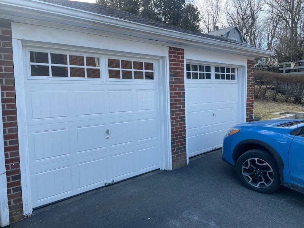 A brick two-car garage with white paneled doors and a blue car parked in the driveway.