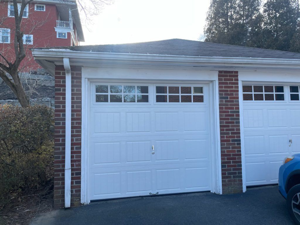 A two-car garage with white paneled doors and rectangular windows, set in a brick building with a gray shingled roof.