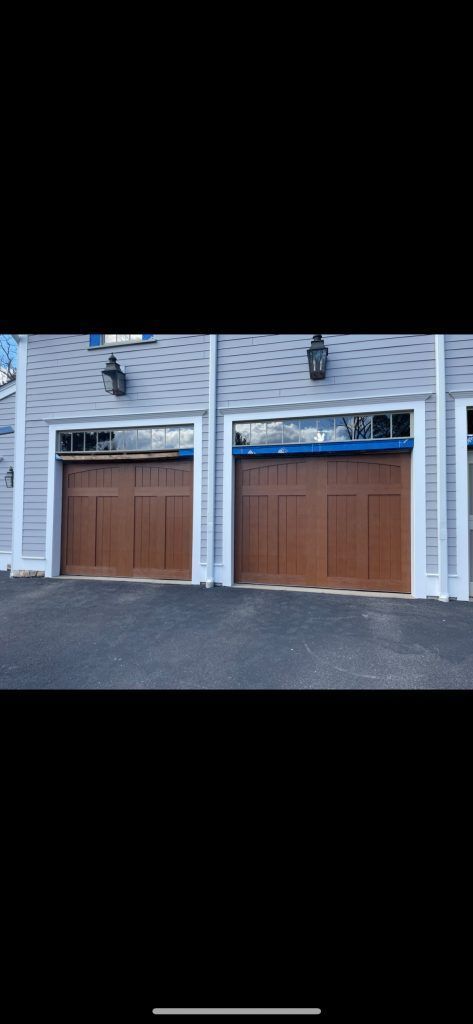 Two wooden carriage-style garage doors with windows on a light-colored house exterior.