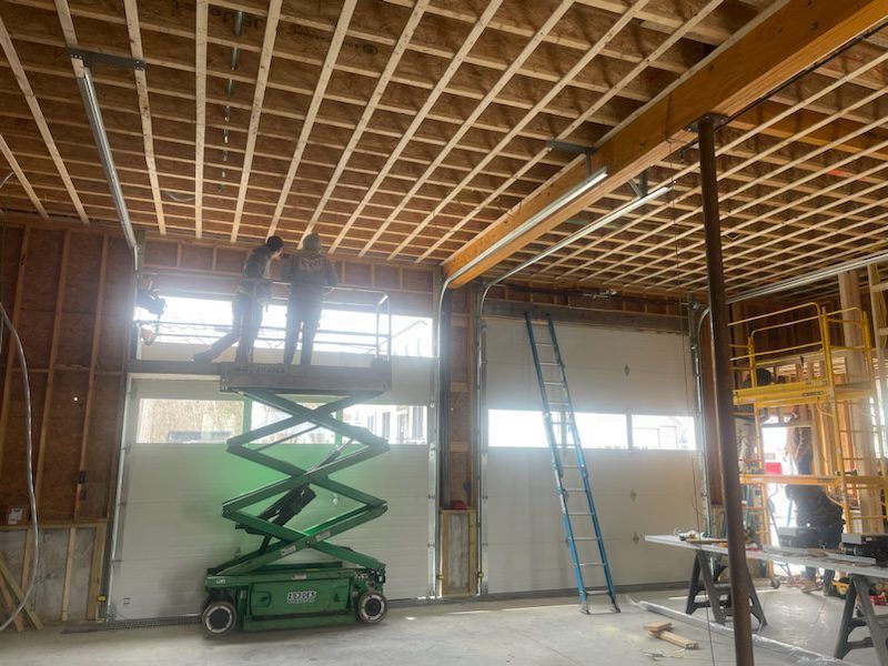 Two workers on a green scissor lift install equipment near the ceiling in a room under construction.