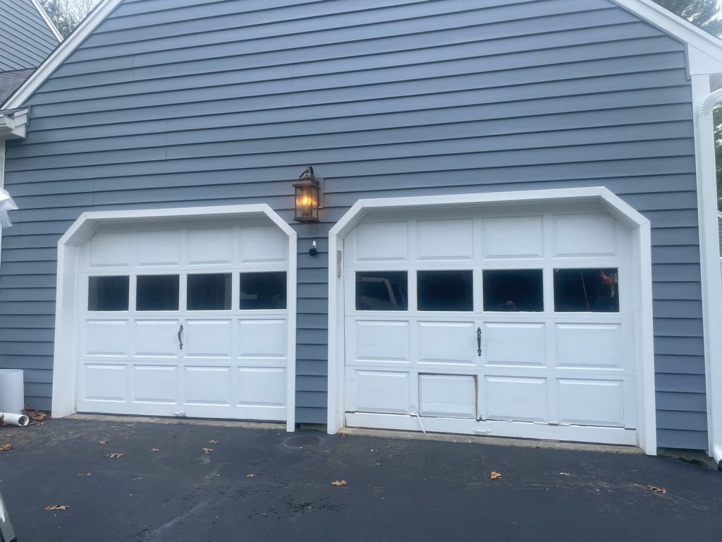 Two white garage doors with glass panels on a building with grey horizontal siding.